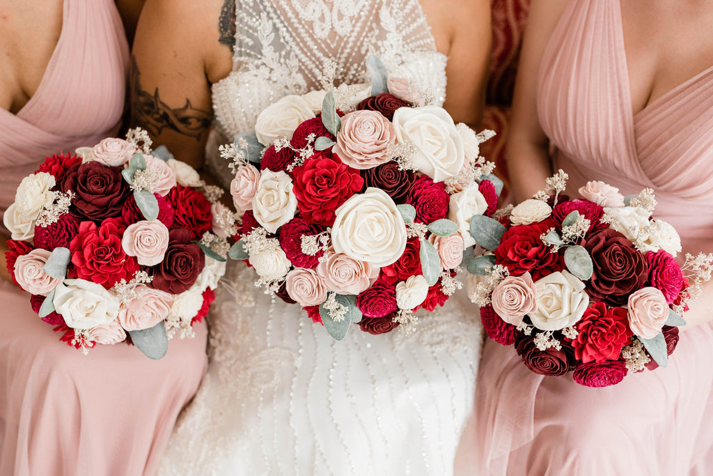 Classic red and burgundy sola wood flower wedding bouquets being held by two bridesmaids in dusty pink and a bride in her wedding gown