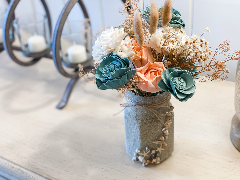 beach inspired mason jar arrangement with delicate sola wood flowers and sand covered mason jar with shells