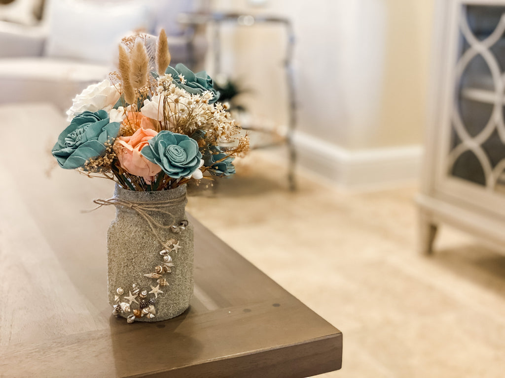 shell and sand covered mason jar arrangement with lasting faux flower arrangement for gifting 
